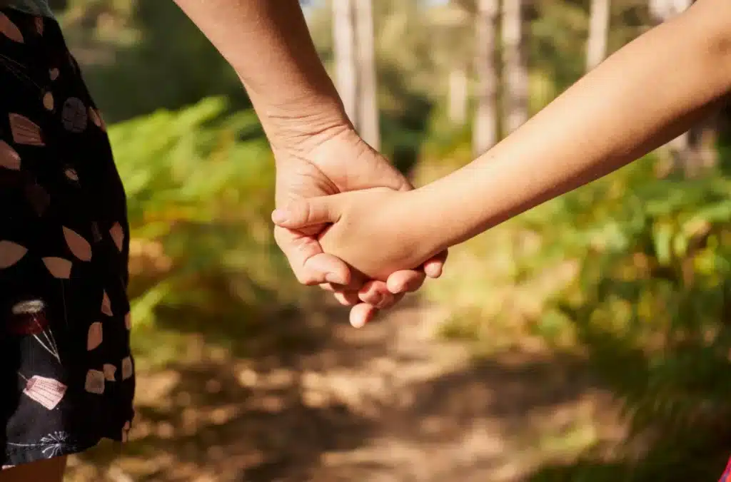 Femme tenant la main d’un enfant sur un chemin, symbole du lien, de la sécurité affective et de l’histoire intérieure.