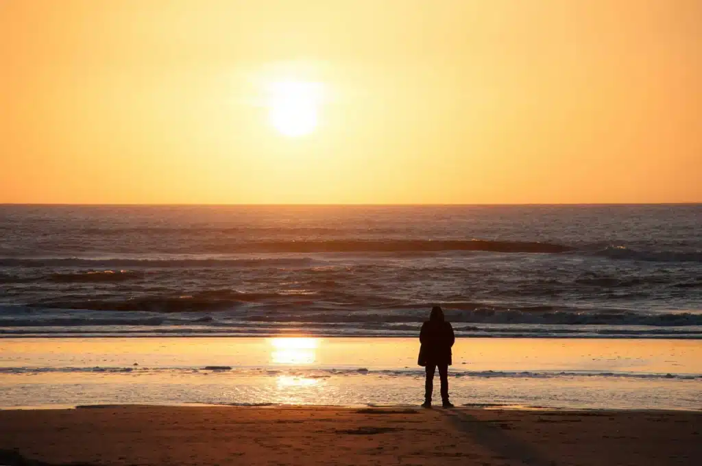 Silhouette contemplant l'océan au lever du soleil, symbole de liberté intérieure, d'apaisement et d'ouverture vers un nouvel horizon.